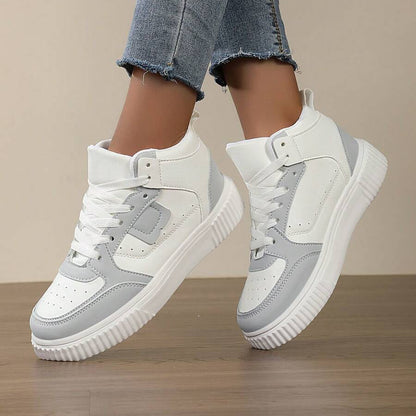 White and gray sneakers worn with blue jeans on a wooden floor.